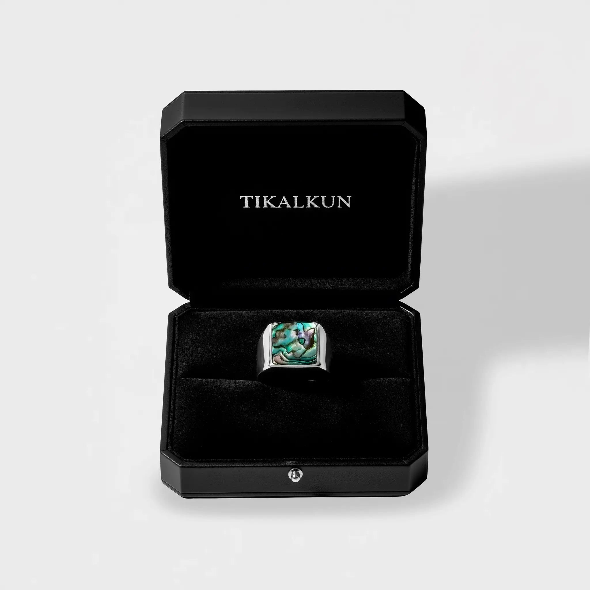 Ring with an abalone shell stone in a black Tikalkun box on a light gray background