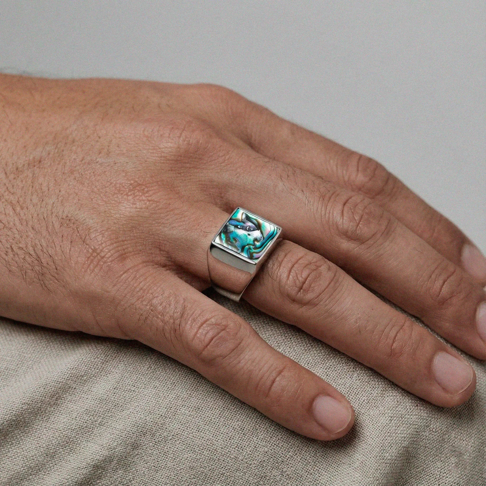 Hand wearing a silver ring with an abalone shell stone on a neutral background