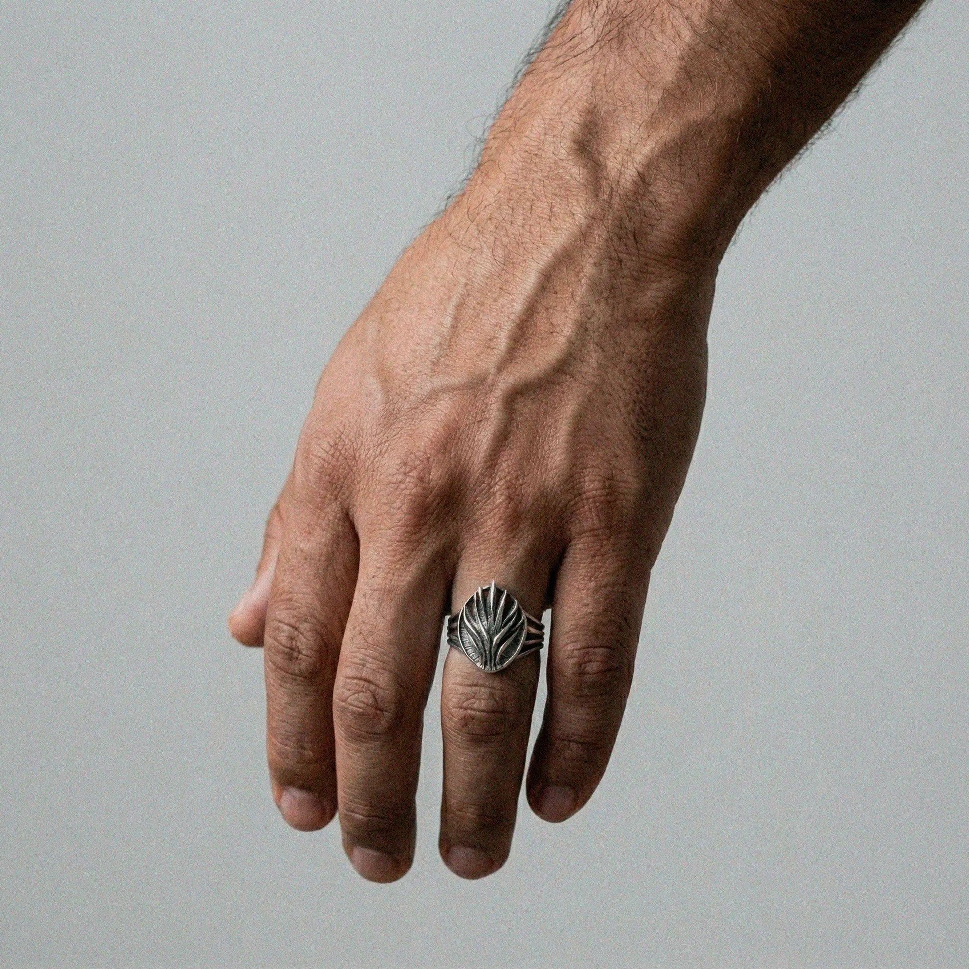 Hand wearing a silver agave ring with a detailed design on a gray background