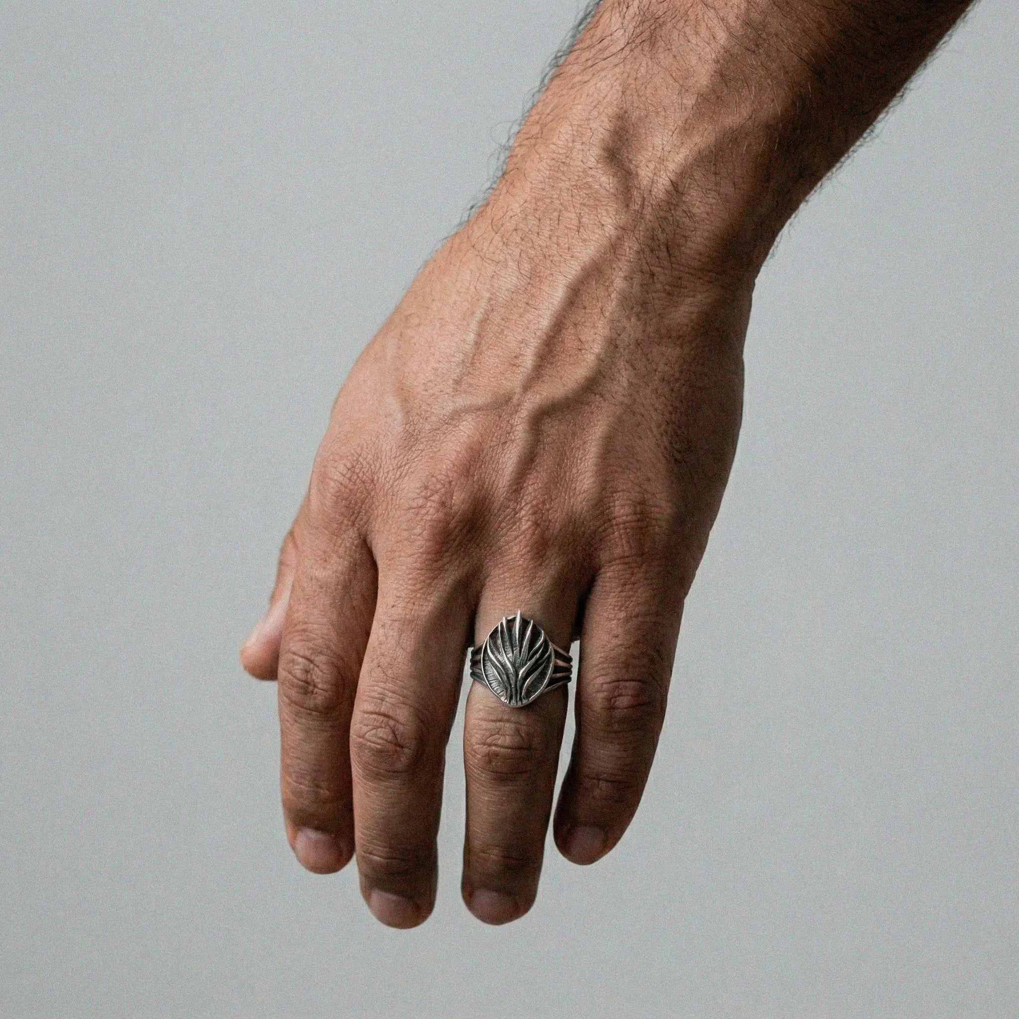 Hand wearing a silver agave ring with a detailed design on a gray background