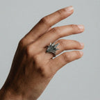Hand wearing a silver Agave-shaped ring on a plain background