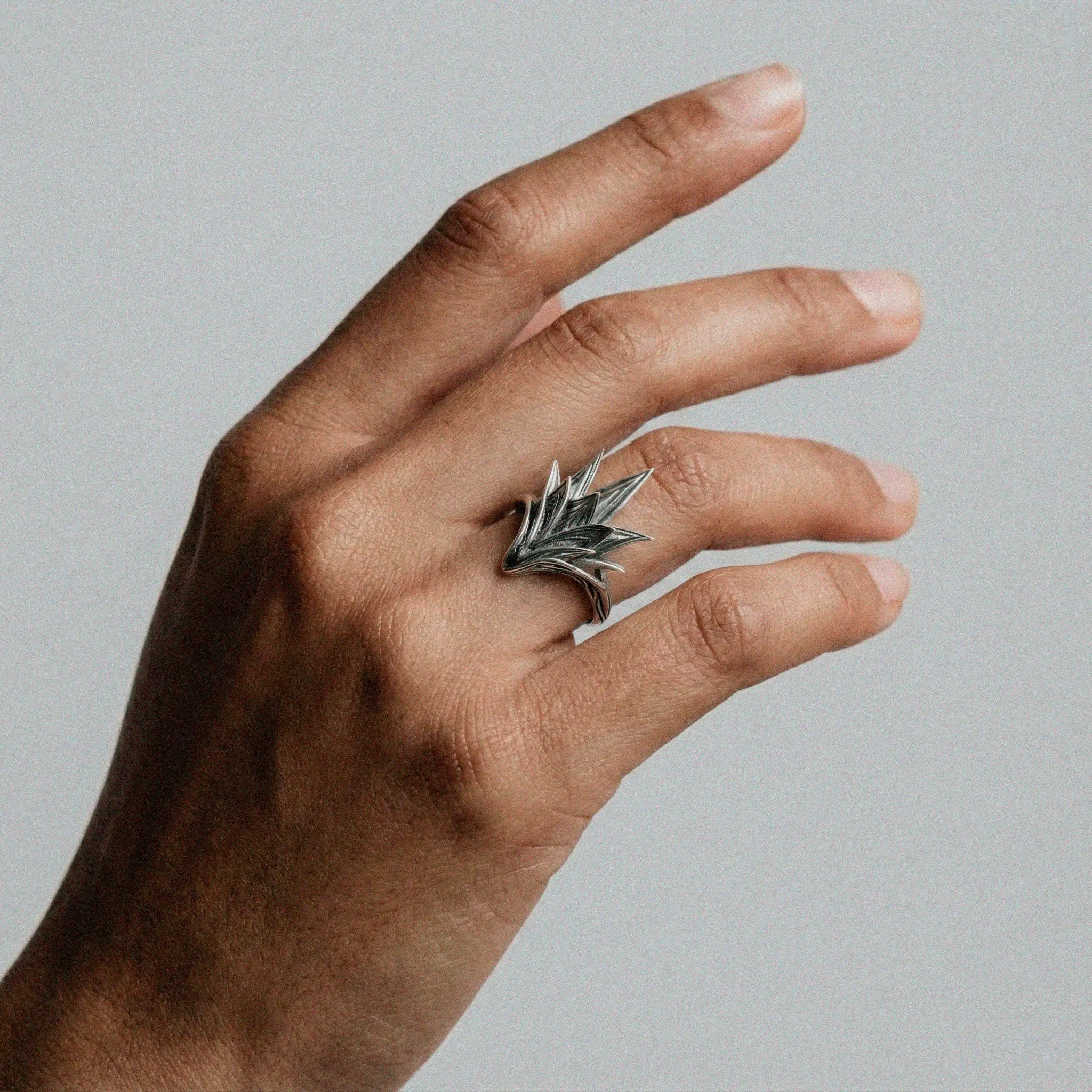 Hand wearing a silver Agave-shaped ring on a plain background