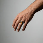 Hand wearing a ring with a amber gemstone on a gray background