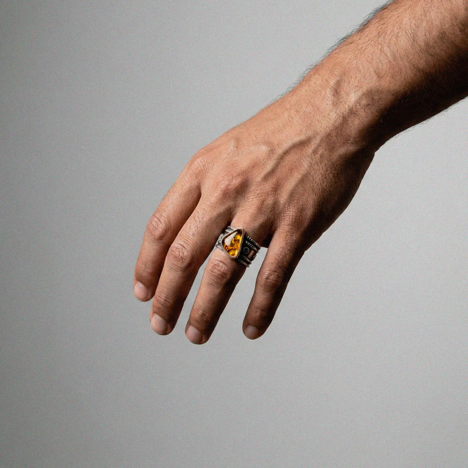 Hand wearing a ring with a amber gemstone on a gray background
