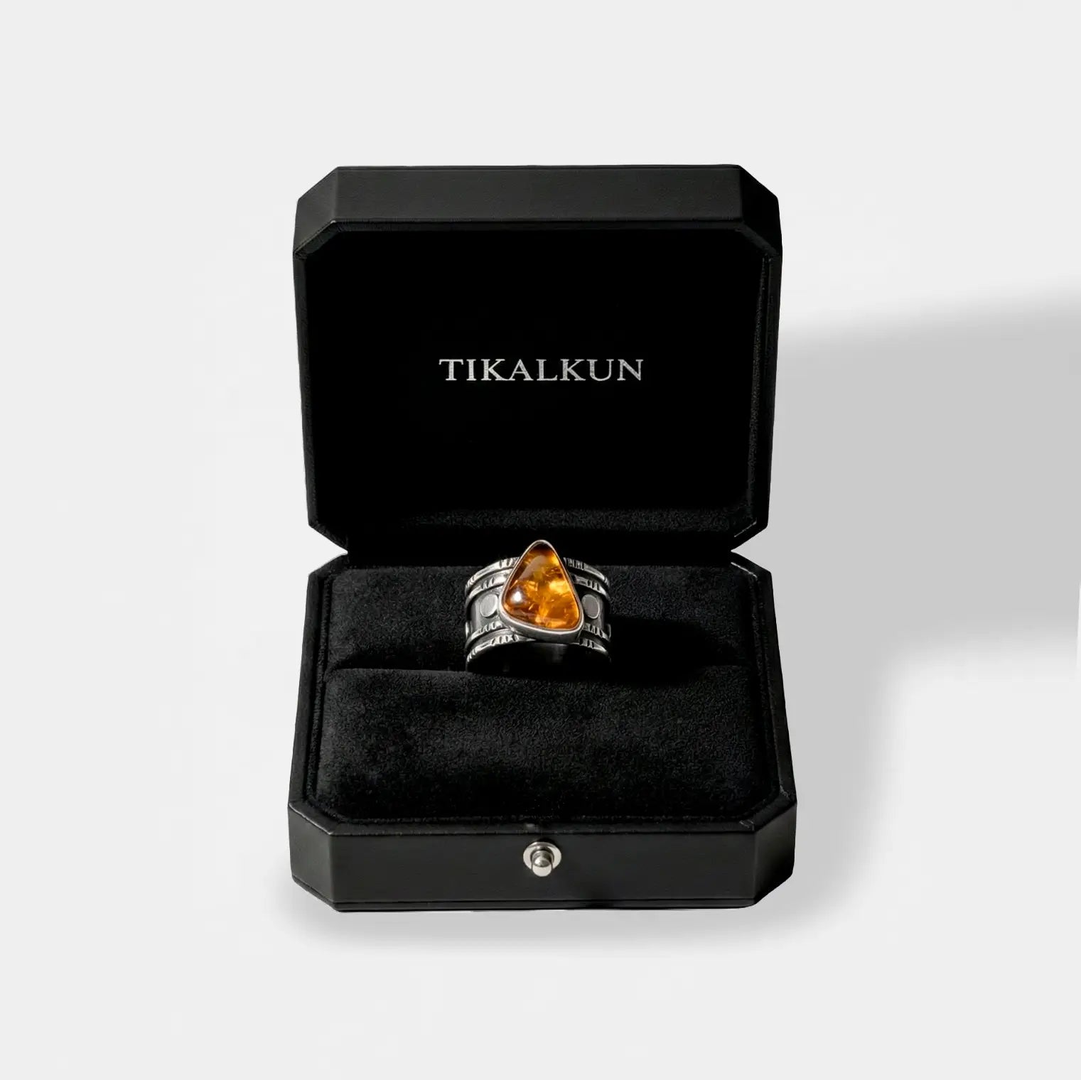 Silver ring with a yellow amber in a black Tikalkun jewelry box on a light gray background