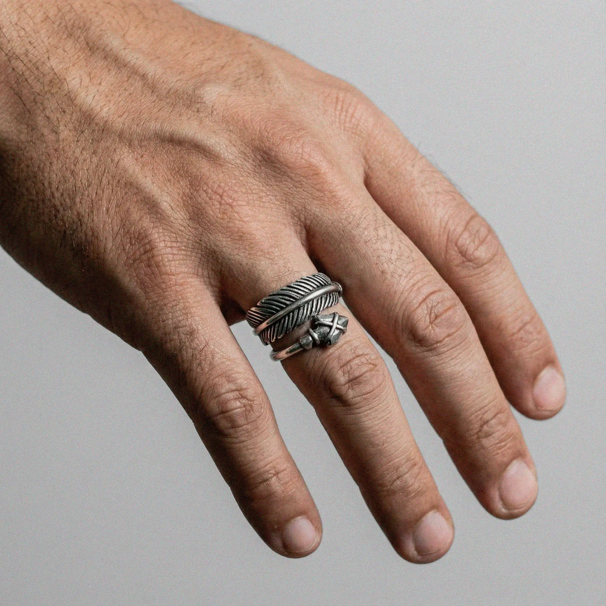 Hand wearing a silver ring with ARROW design on a gray background