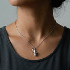 Person wearing a silver necklace with a small axolotl pendant against a neutral background