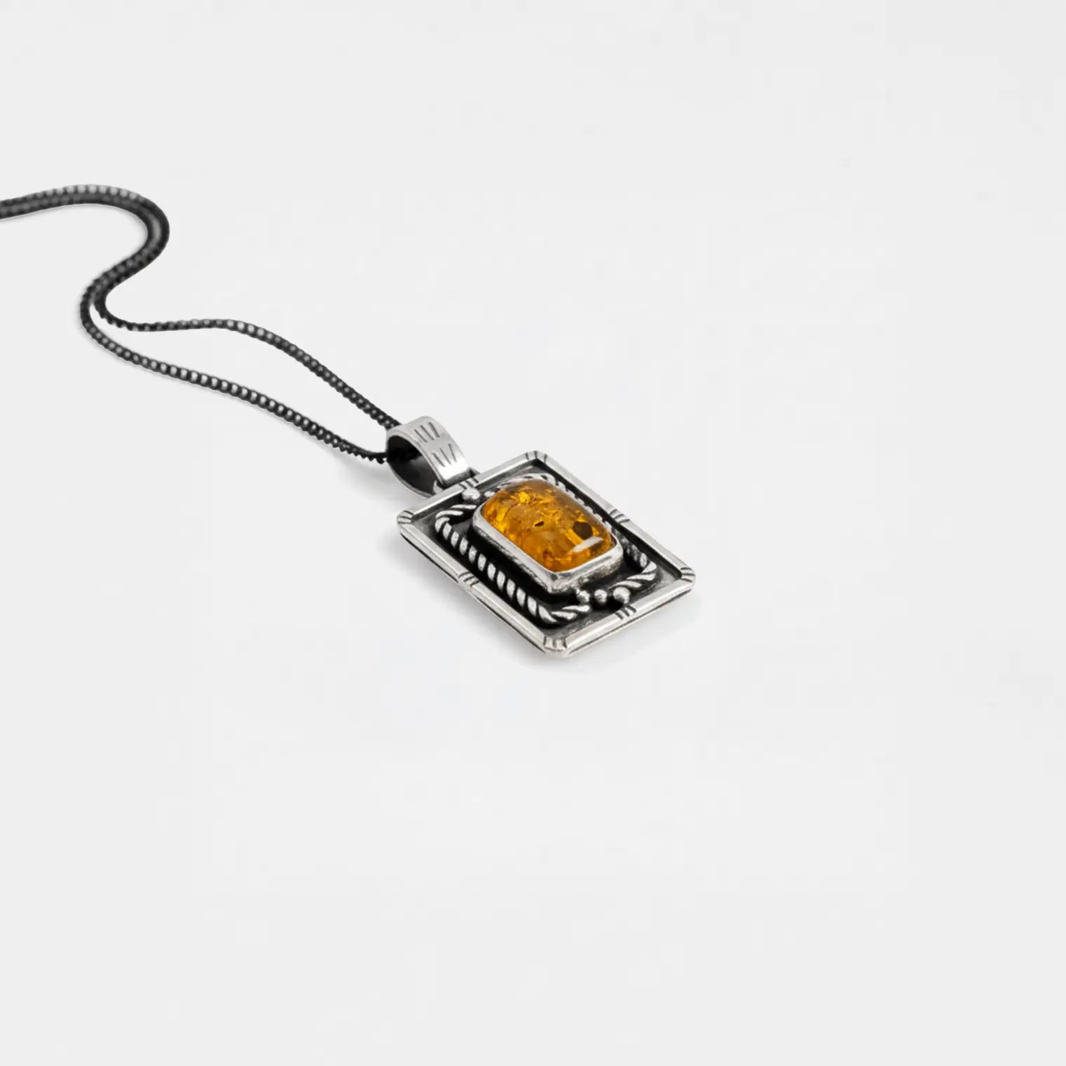 Silver pendant with a rectangular amber stone on a white background