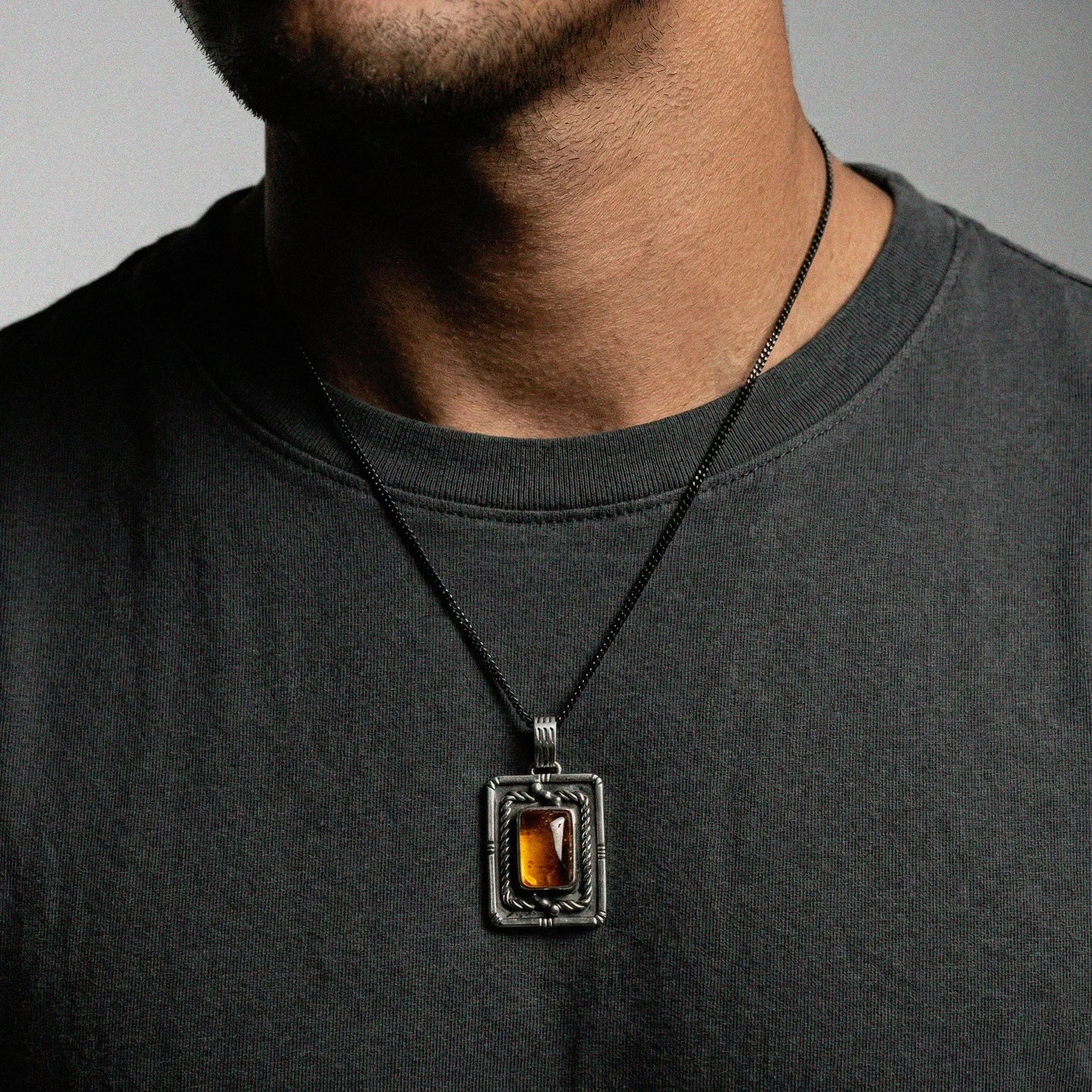 Man wearing a dark gray shirt with a necklace featuring a rectangular pendant.