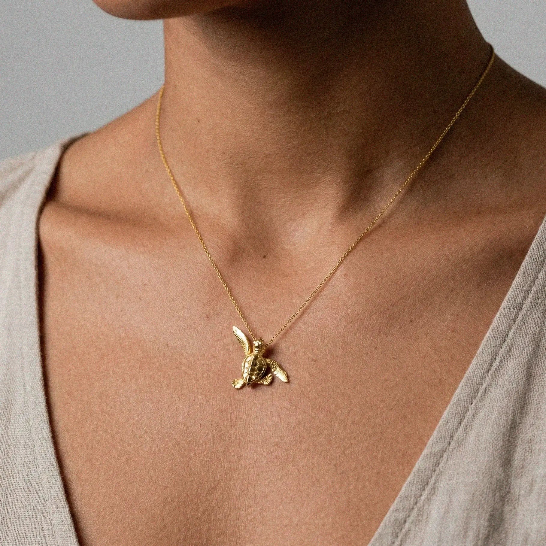 woman wearing a baby turtle gold pendant on a white background