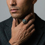 Man wearing a ring with a jaguar design, touching his neck against a neutral background
