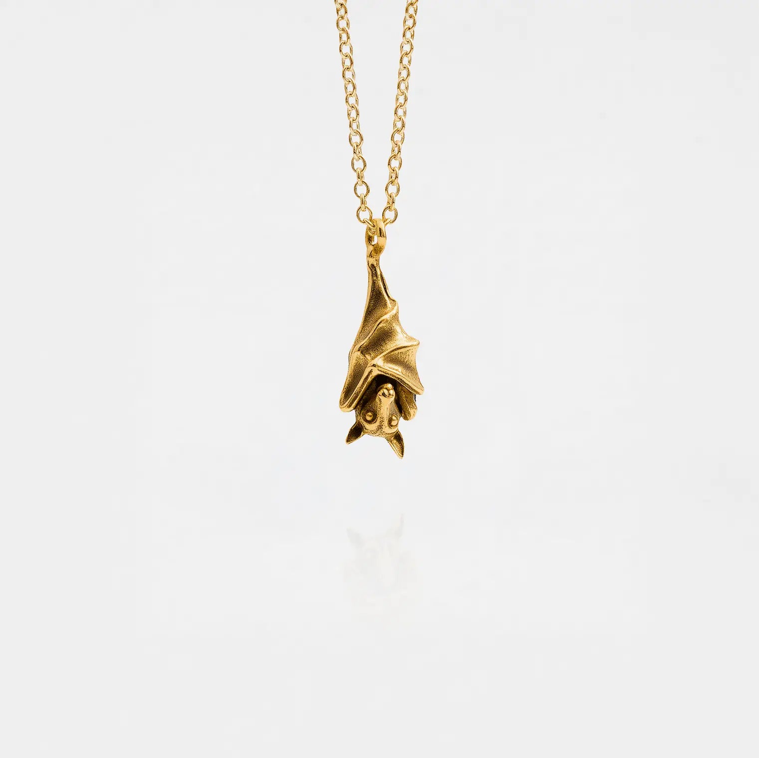 Gold bat pendant necklace on a white background