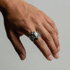 Hand wearing a silver ring with a bat design on a neutral background