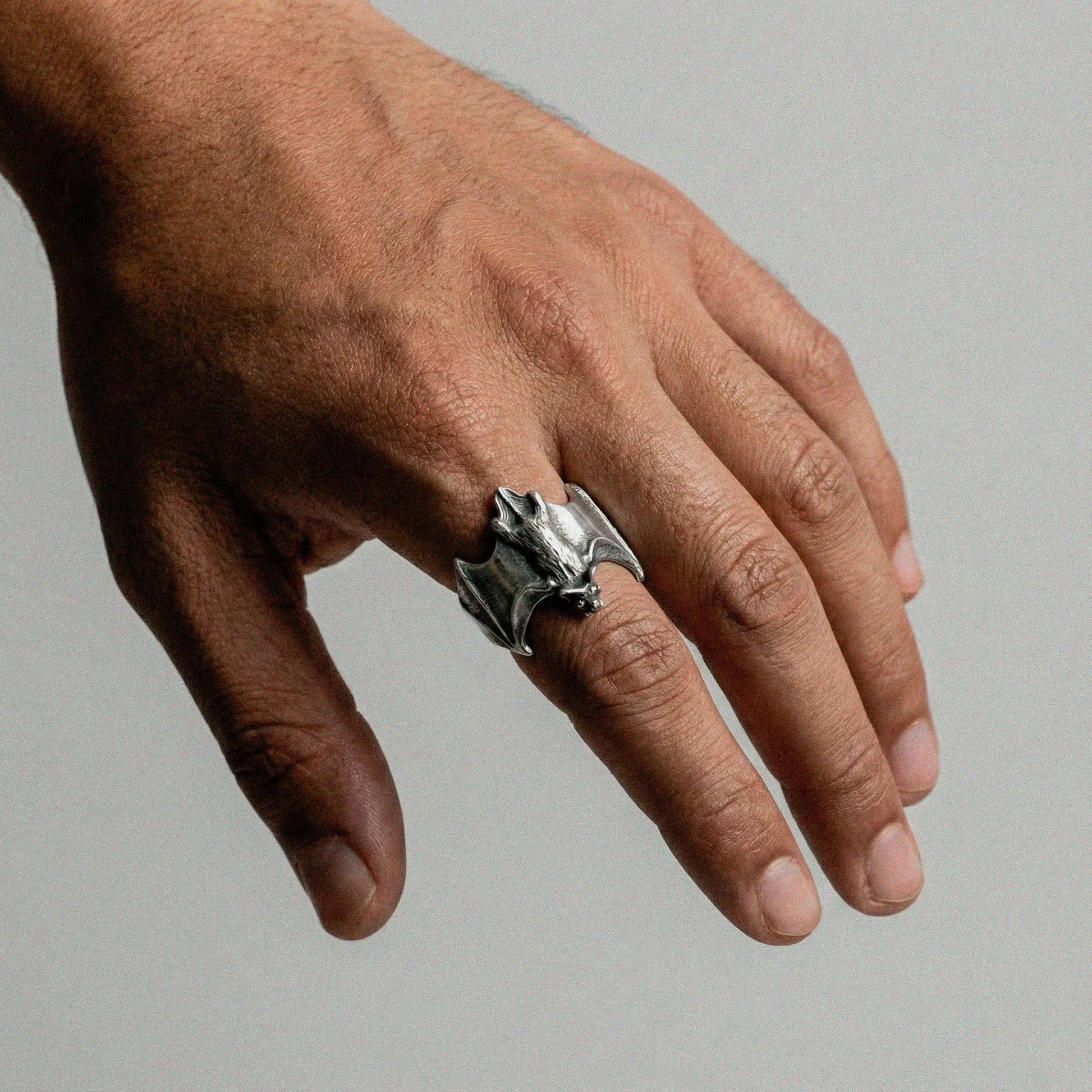 Hand wearing a silver ring with a bat design on a neutral background