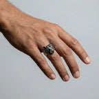Hand wearing a silver ring with a BEAR design on a plain background