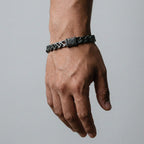Hand wearing a black braided bracelet on a gray background