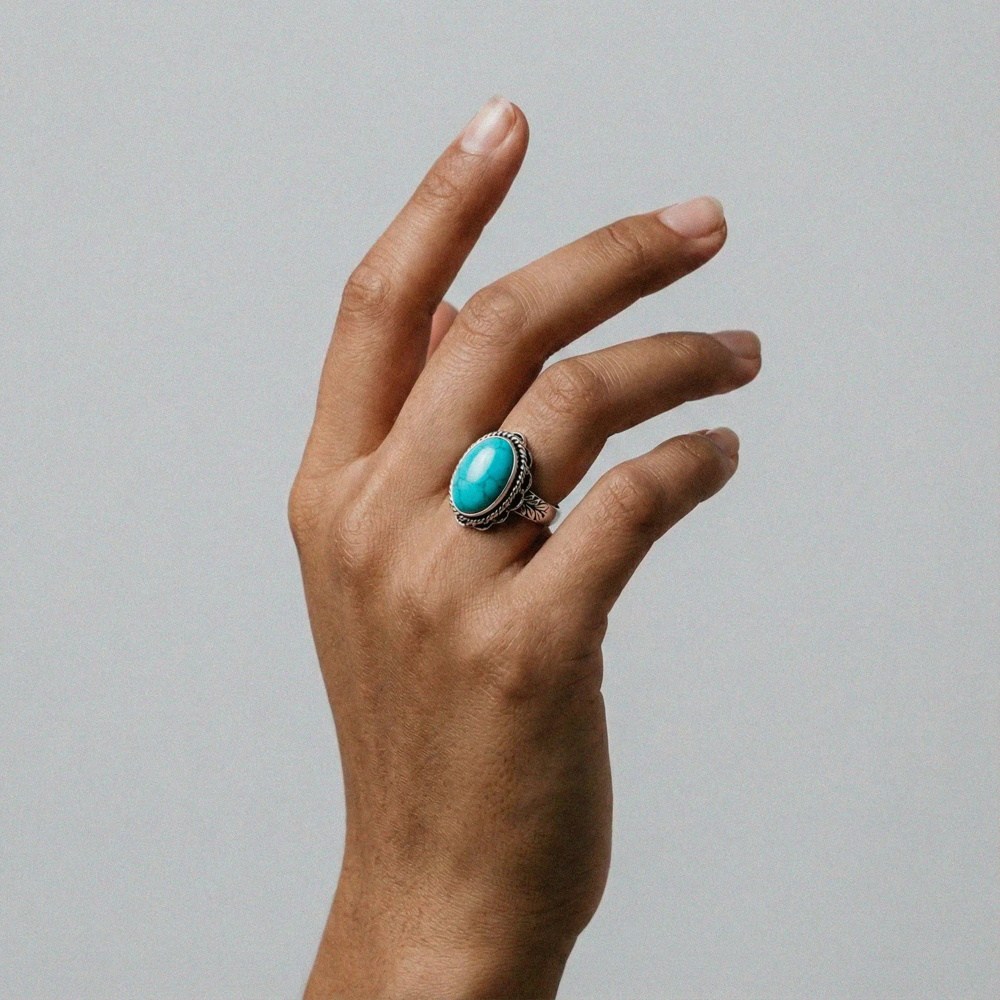 Hand wearing a turquoise ring on a plain background