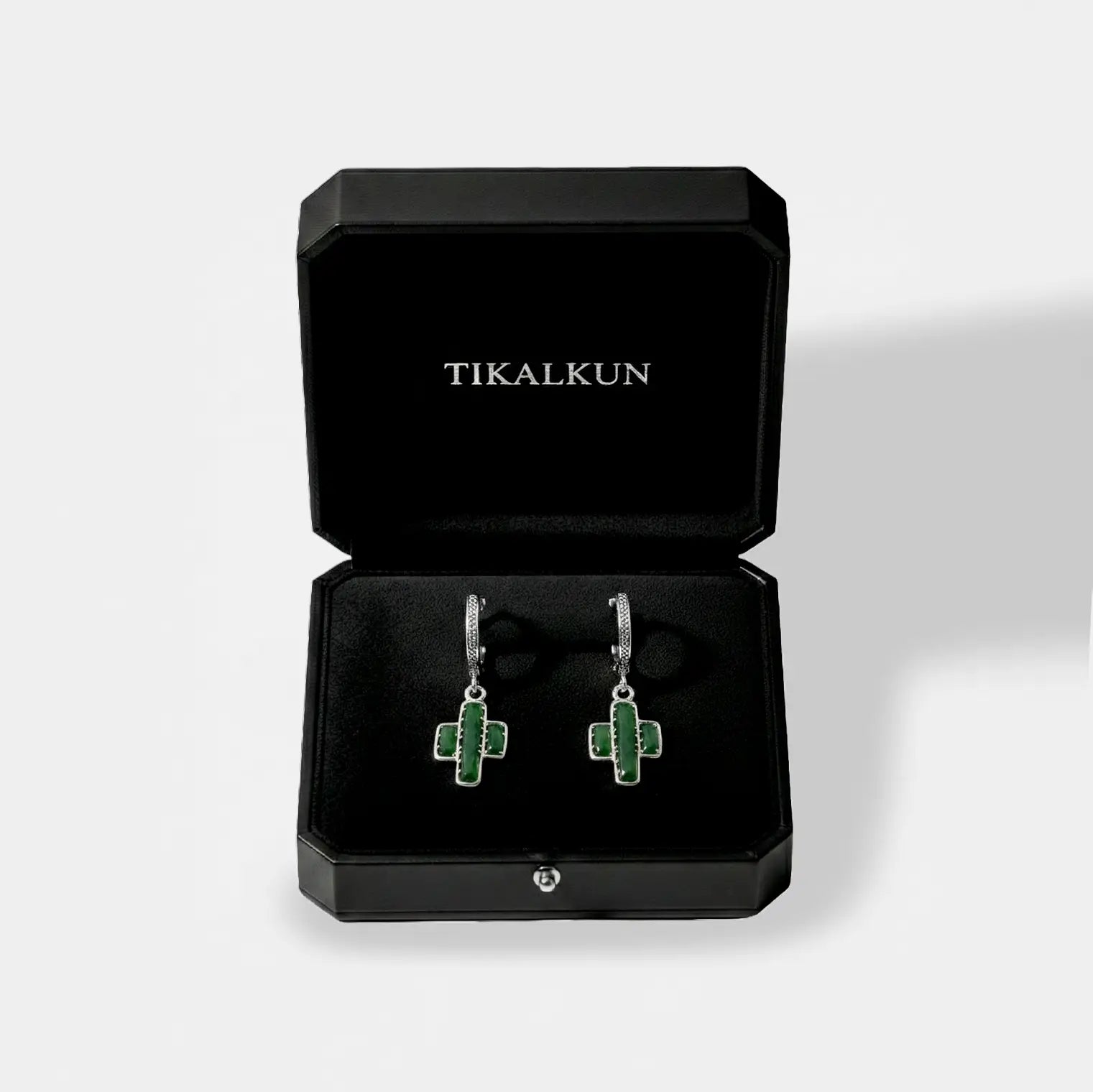 Green cactus earrings in a black Tikalkun jewelry box on a light gray background