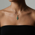 Necklace with a cactus-shaped pendant on a person wearing a black top against a neutral background