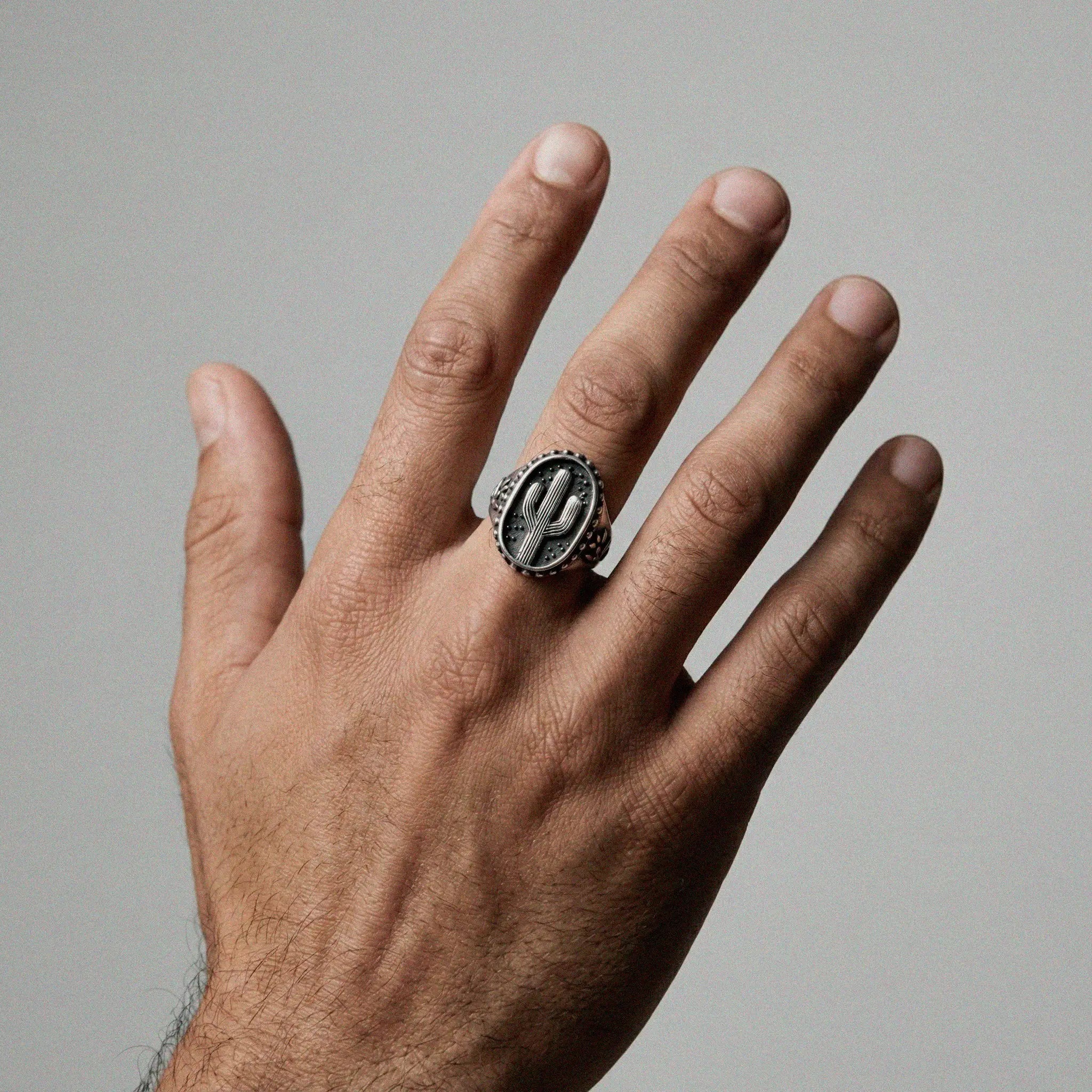 Hand wearing a silver cactus ring  on a gray background