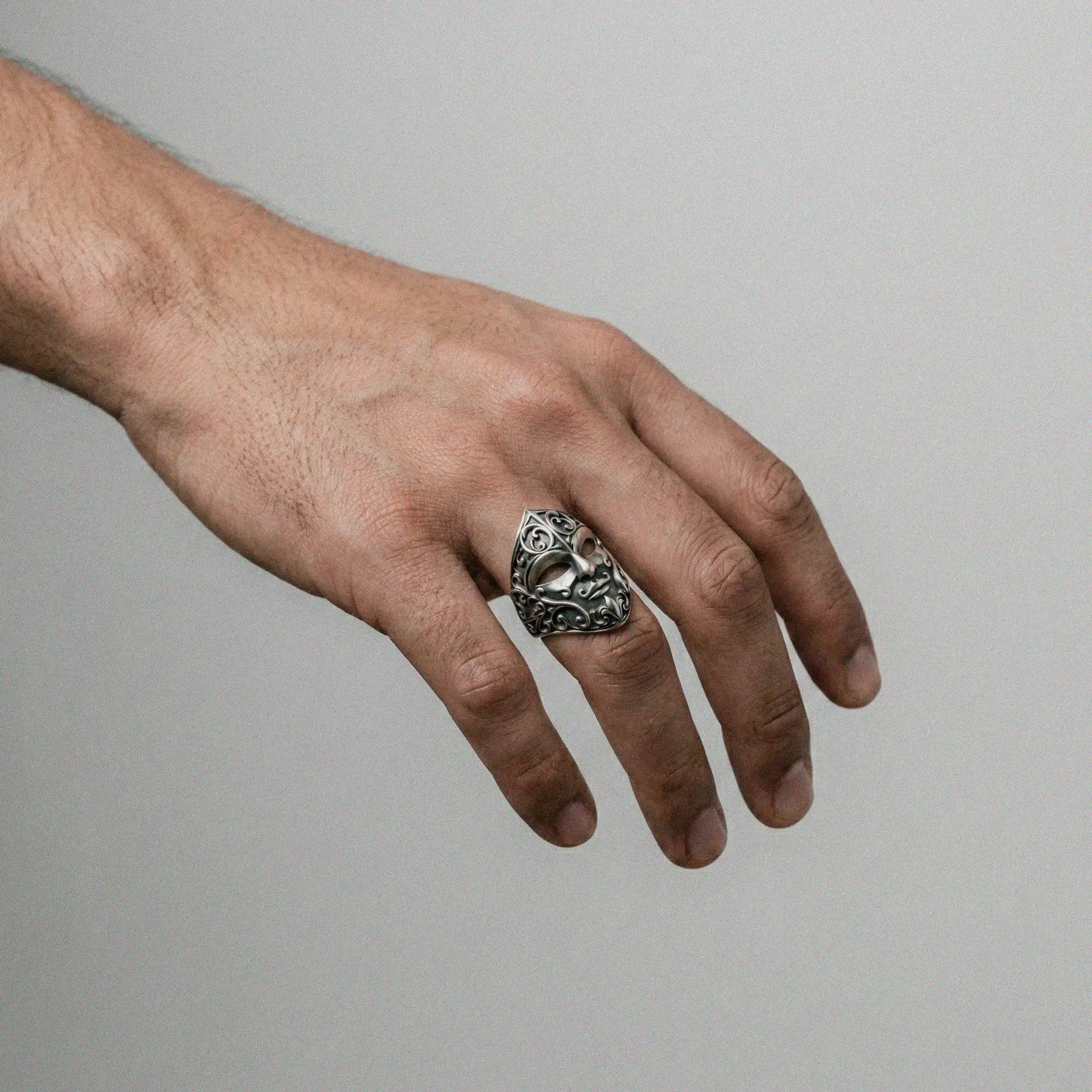 Man's hand wearing a Silver carnival mask ring on a white background