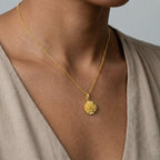 marigold flower Gold necklace with a pendant on a person wearing a beige top against a neutral background