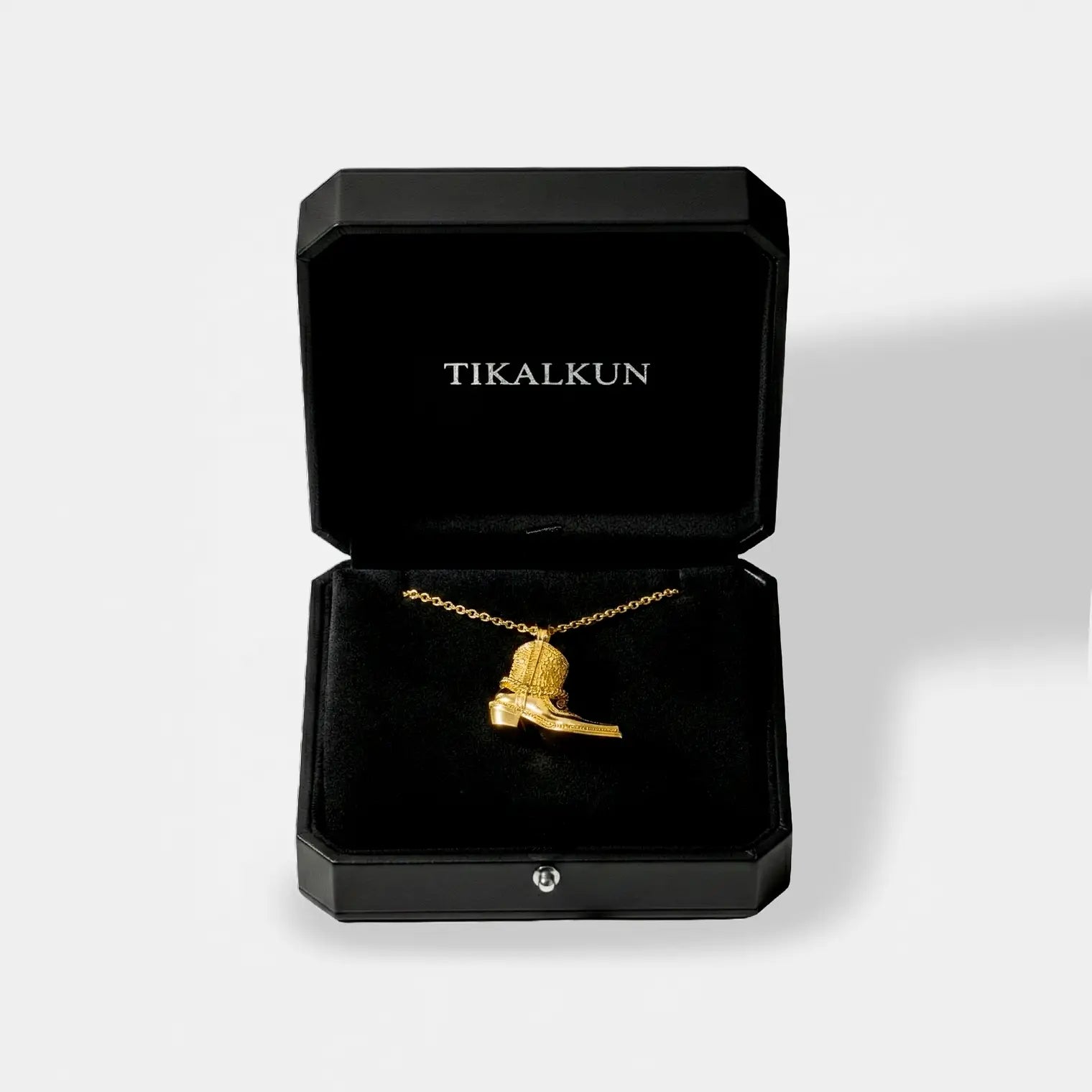 black "TIKALKUN" jewelry box with a gold cowboy boot pendant isnide it,  on a white background