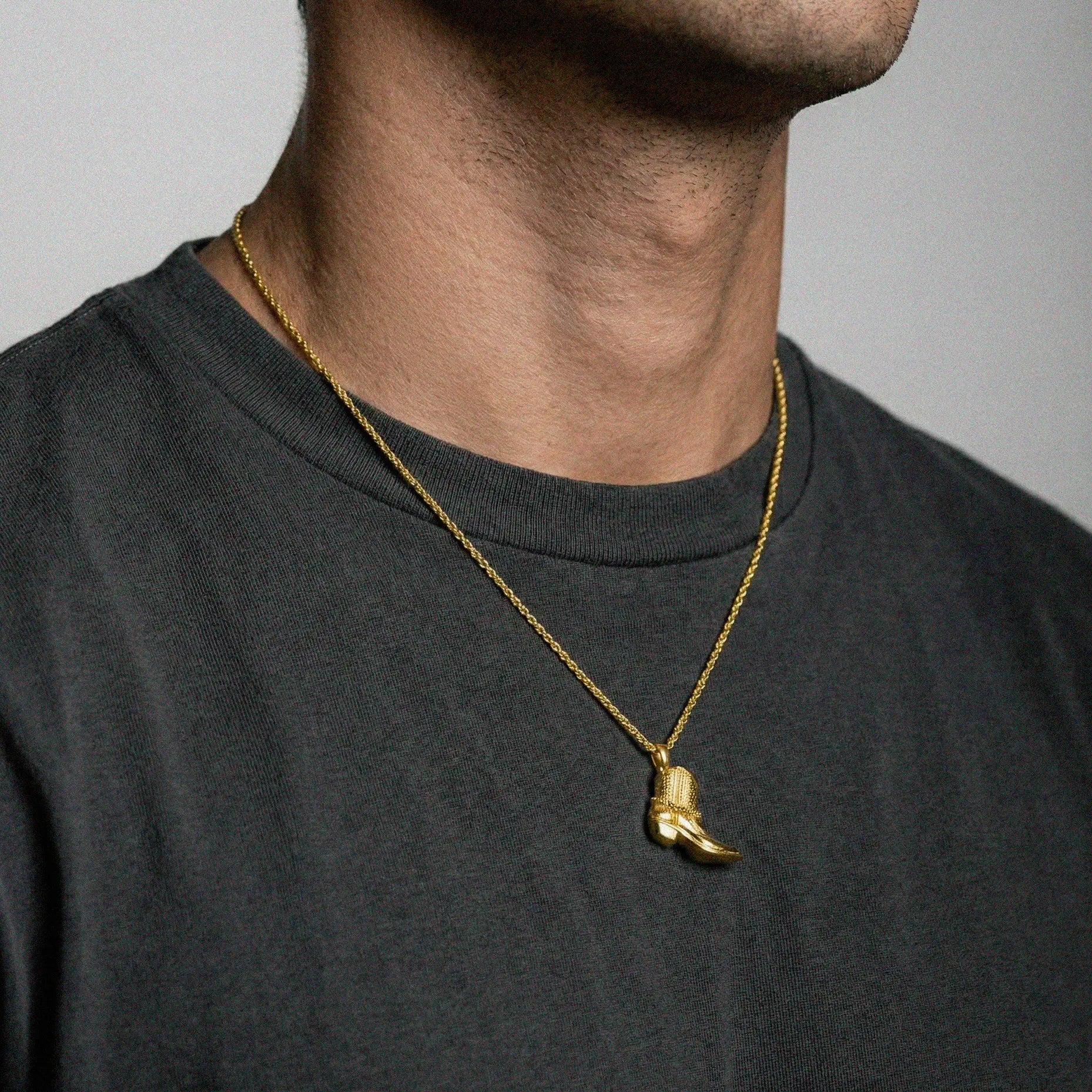 person wearing a gold cowboy boot pendant on a gray background