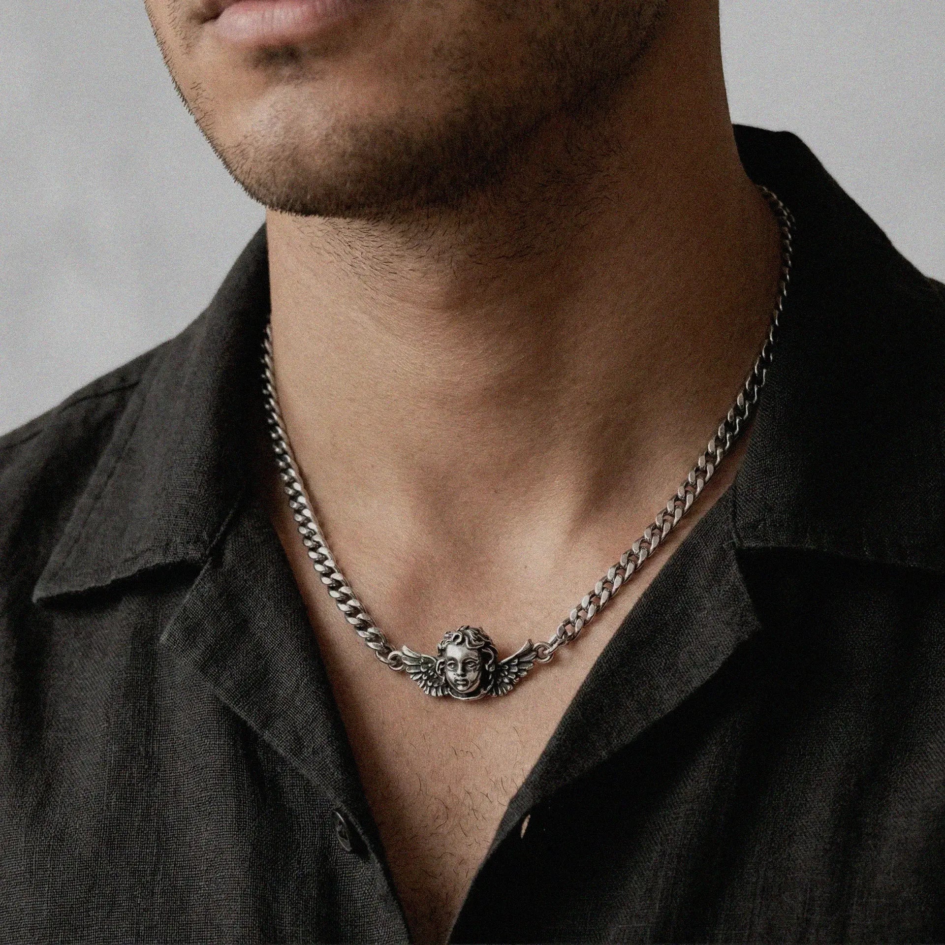 person wearing a silver necklace featuring a cherub design 