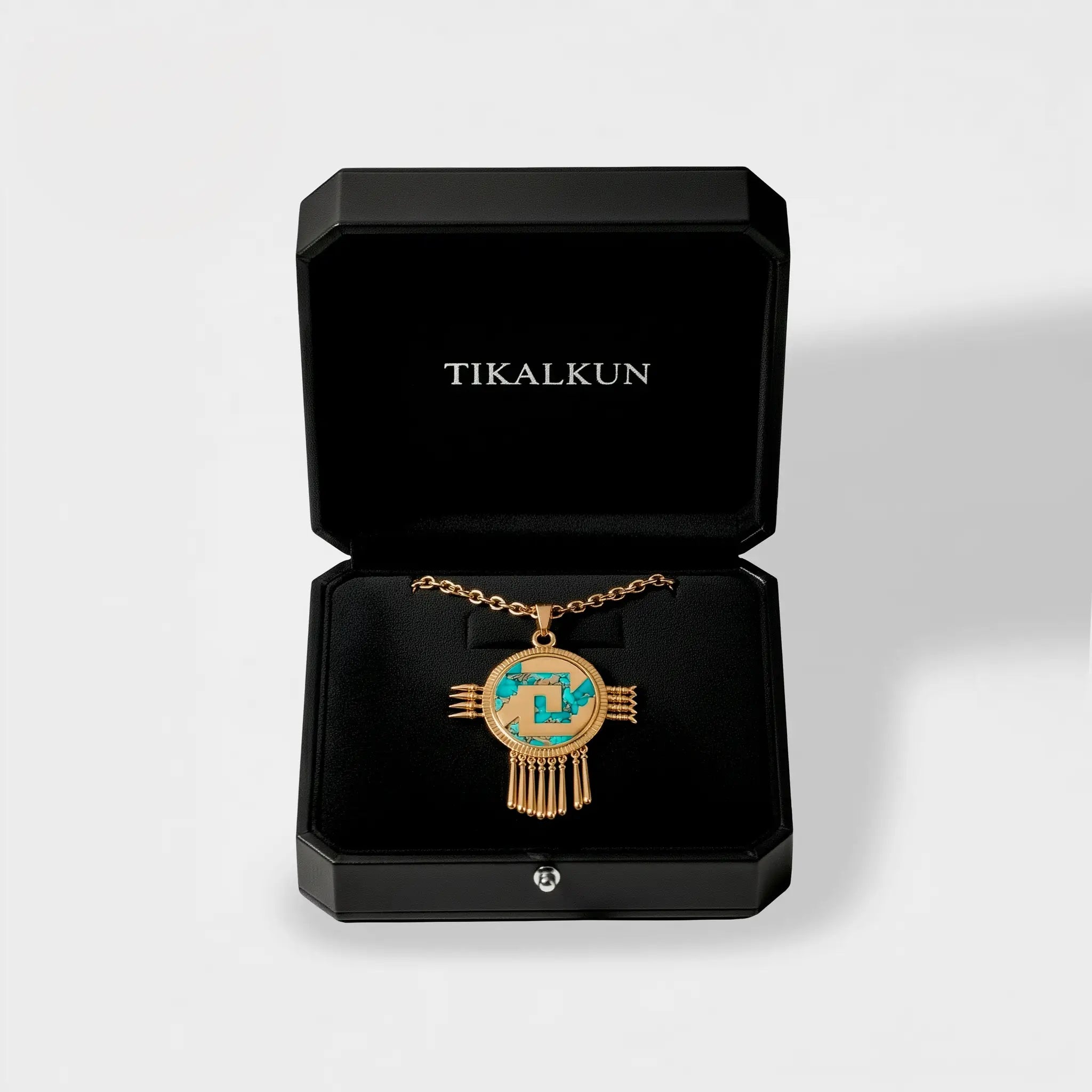 aztec shield Gold necklace with turquoise stones in a black 'TIKALKUN' box on a light gray background