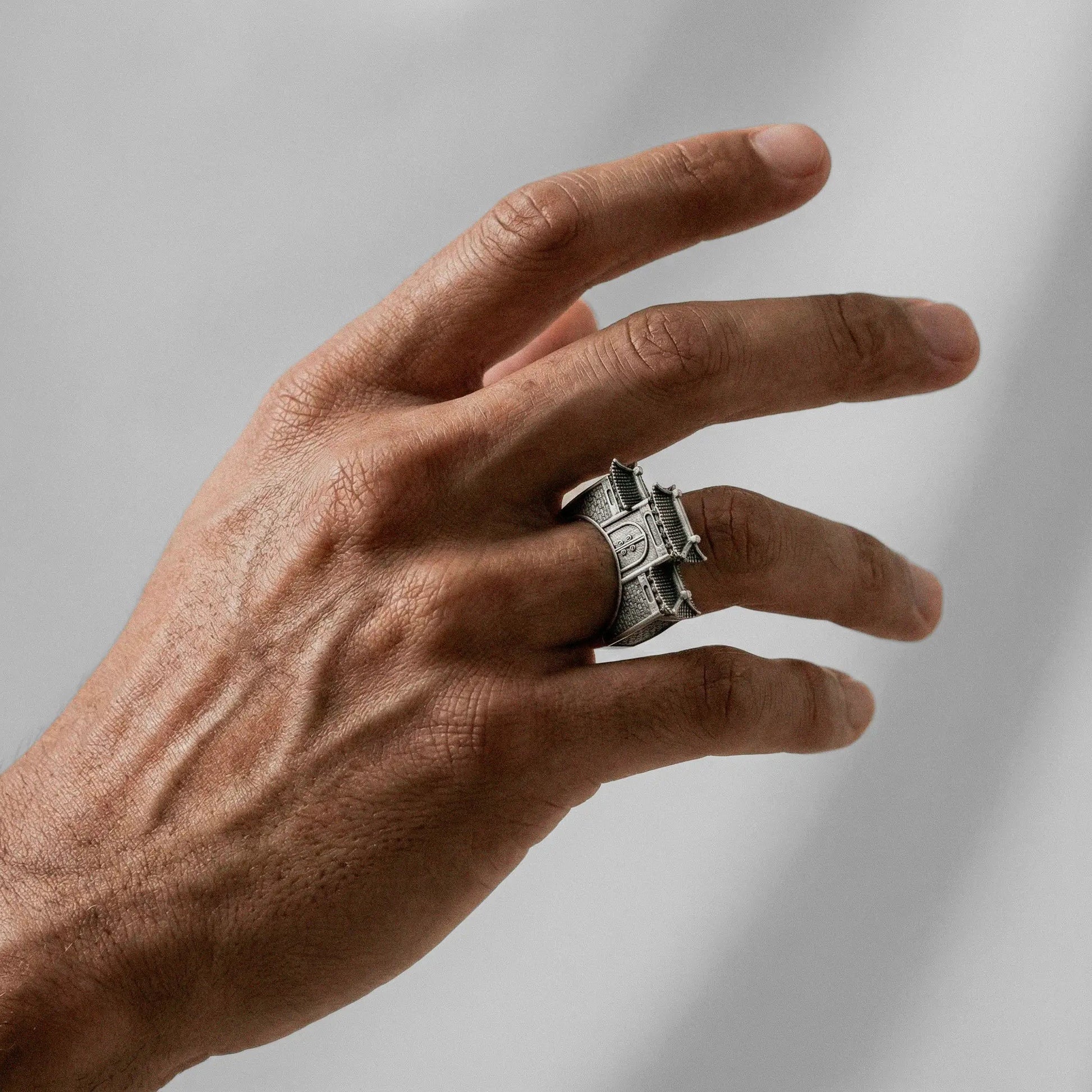 Hand wearing a silver CHINESE ARCHITECTURE ring on a plain background
