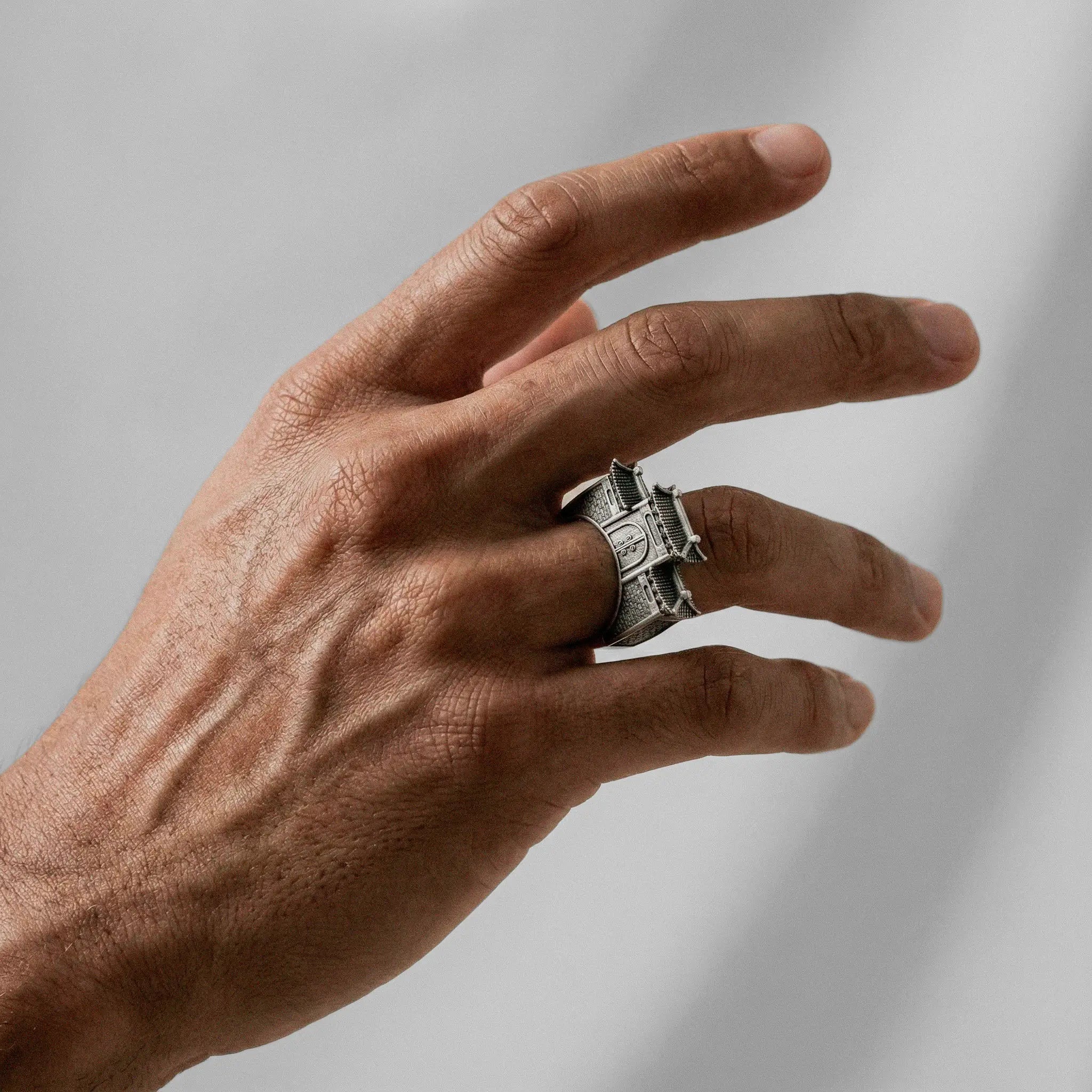 Hand wearing a silver CHINESE ARCHITECTURE ring on a plain background