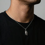 Person wearing a black shirt with a silver necklace featuring a corn pendant.