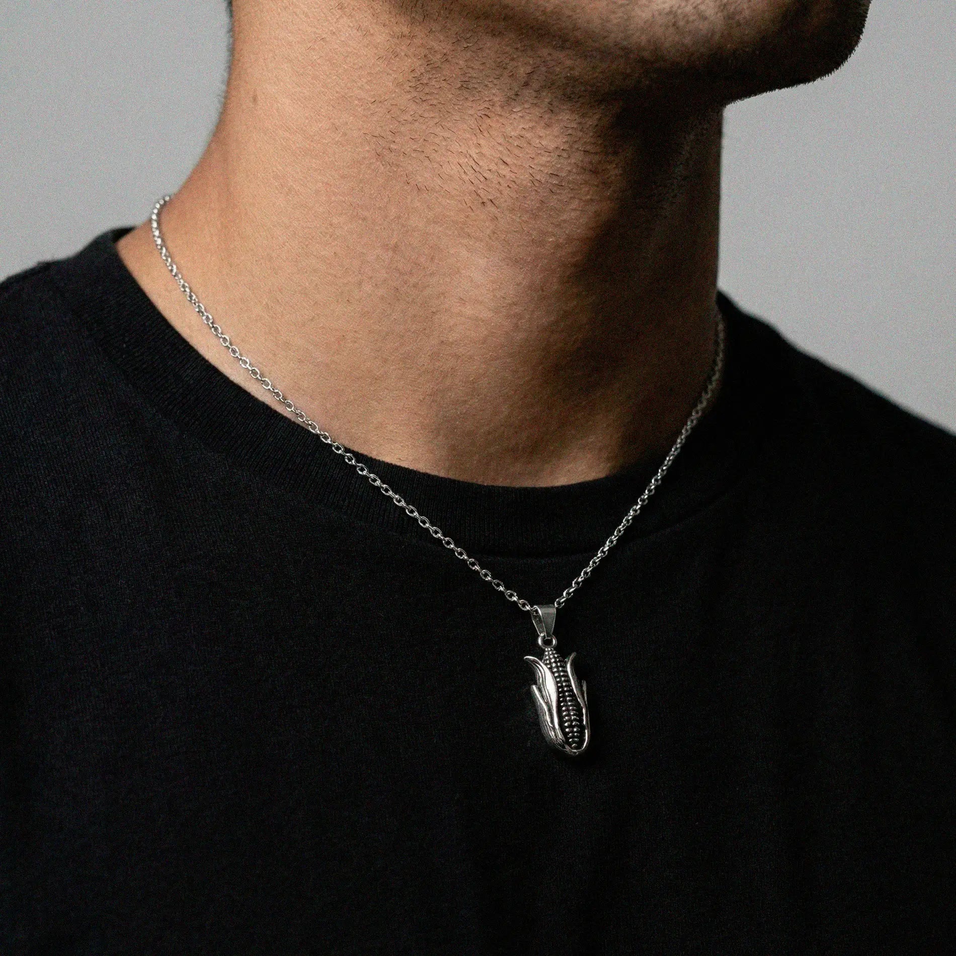 Person wearing a black shirt with a silver necklace featuring a corn pendant.