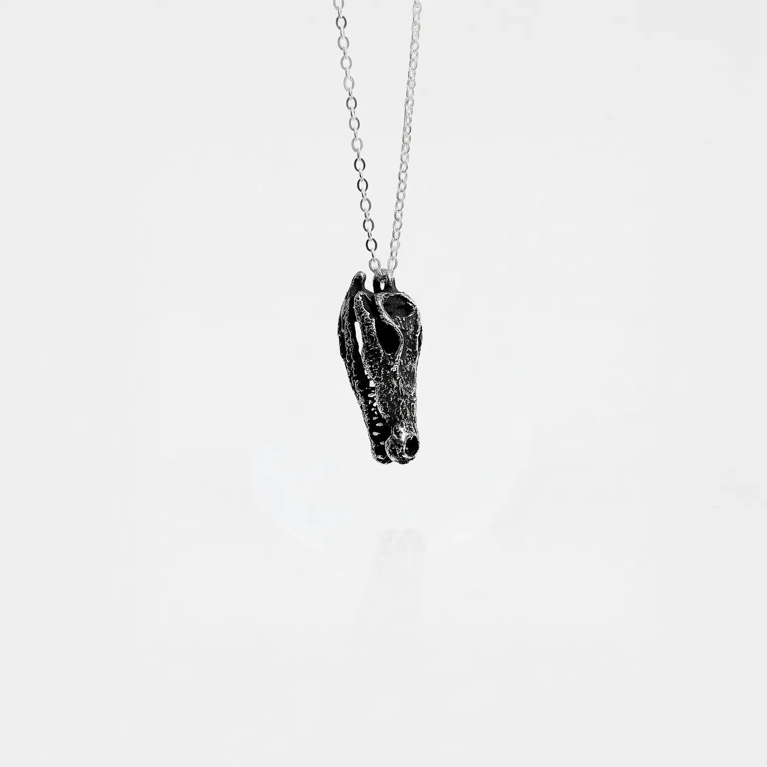 Silver necklace with a crocodile skull pendant on a white background