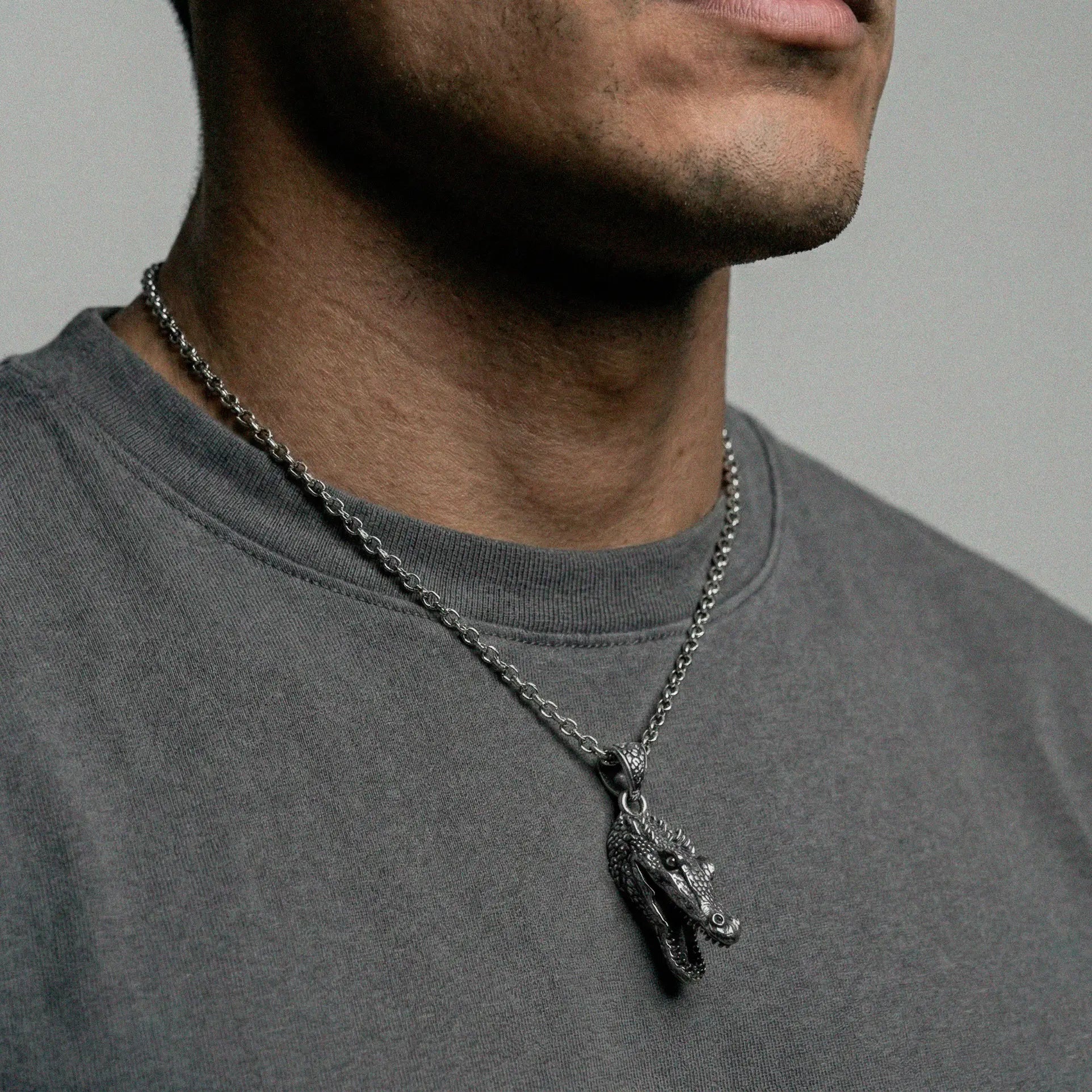 Man wearing a necklace with a crocodile pendant on a plain background