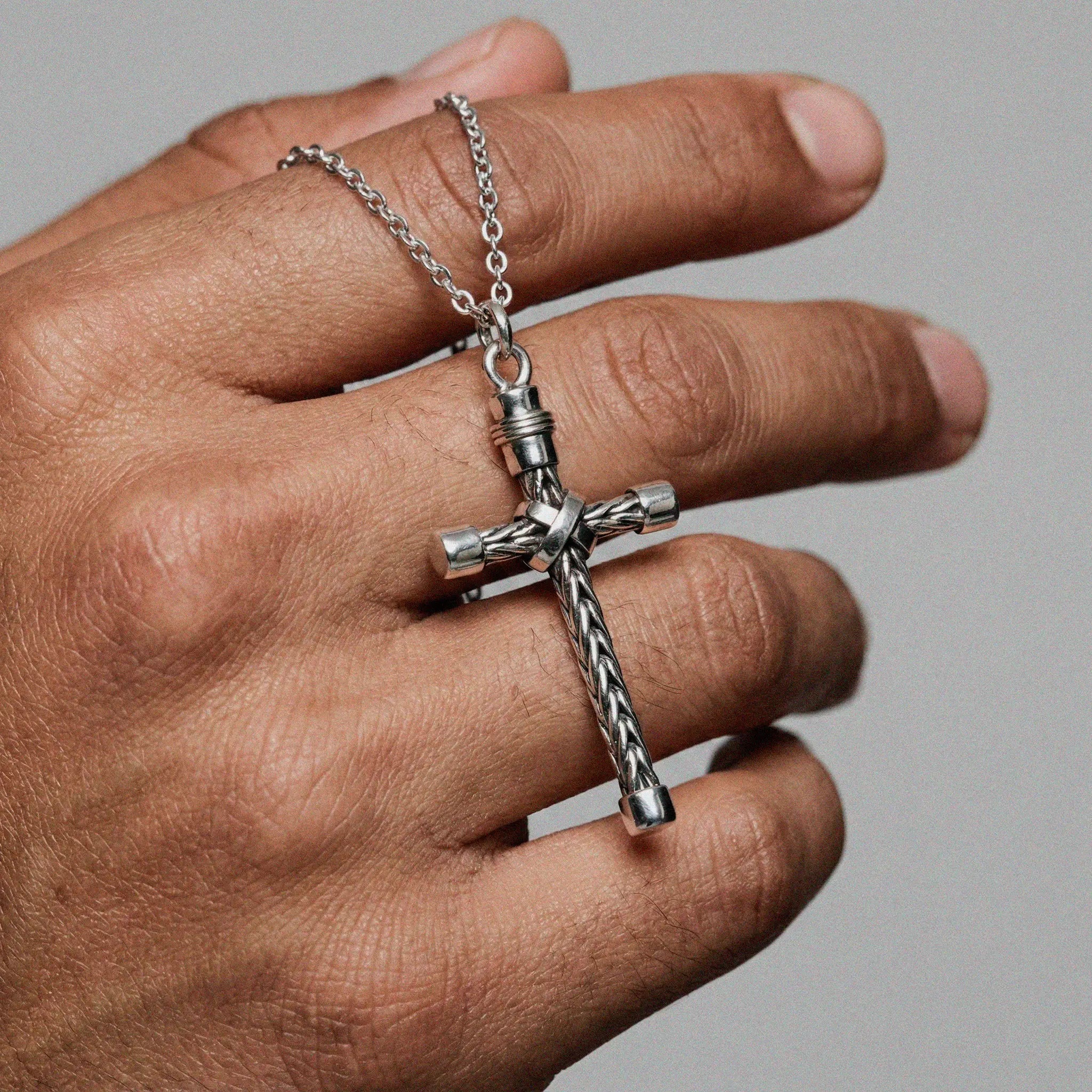 Silver cross pendant necklace on a hand against a gray background