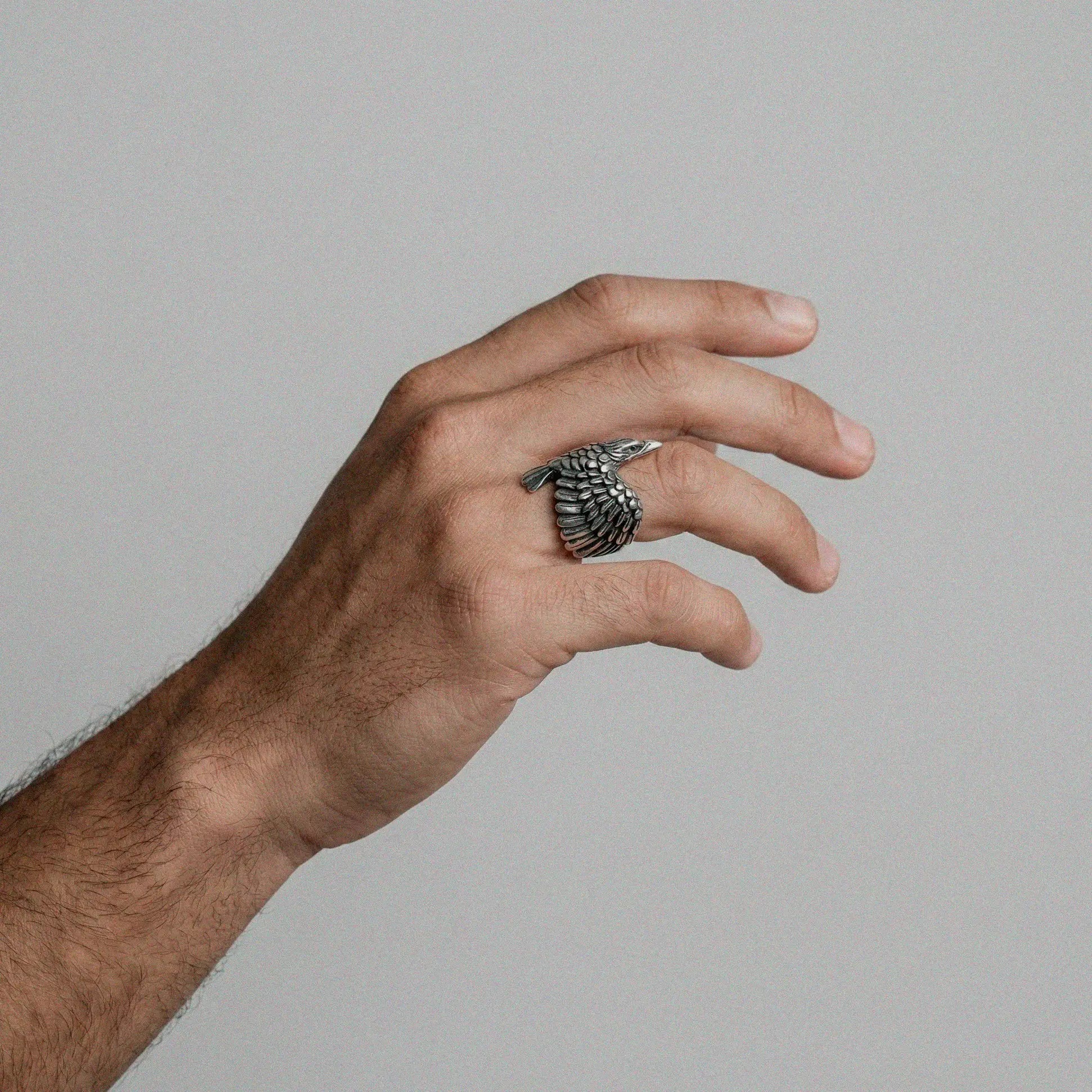 Hand wearing a silver crow ring on a plain background