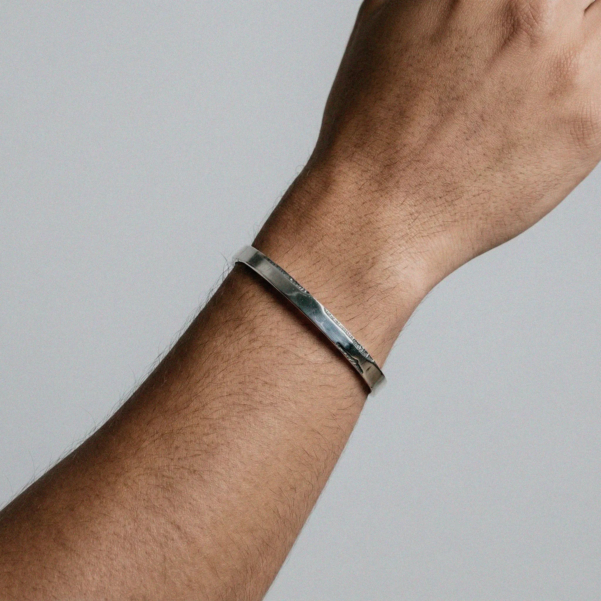 Silver bracelet on a wrist against a neutral background