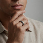 Man wearing a silver ring with skulls design, resting his chin on his hand.