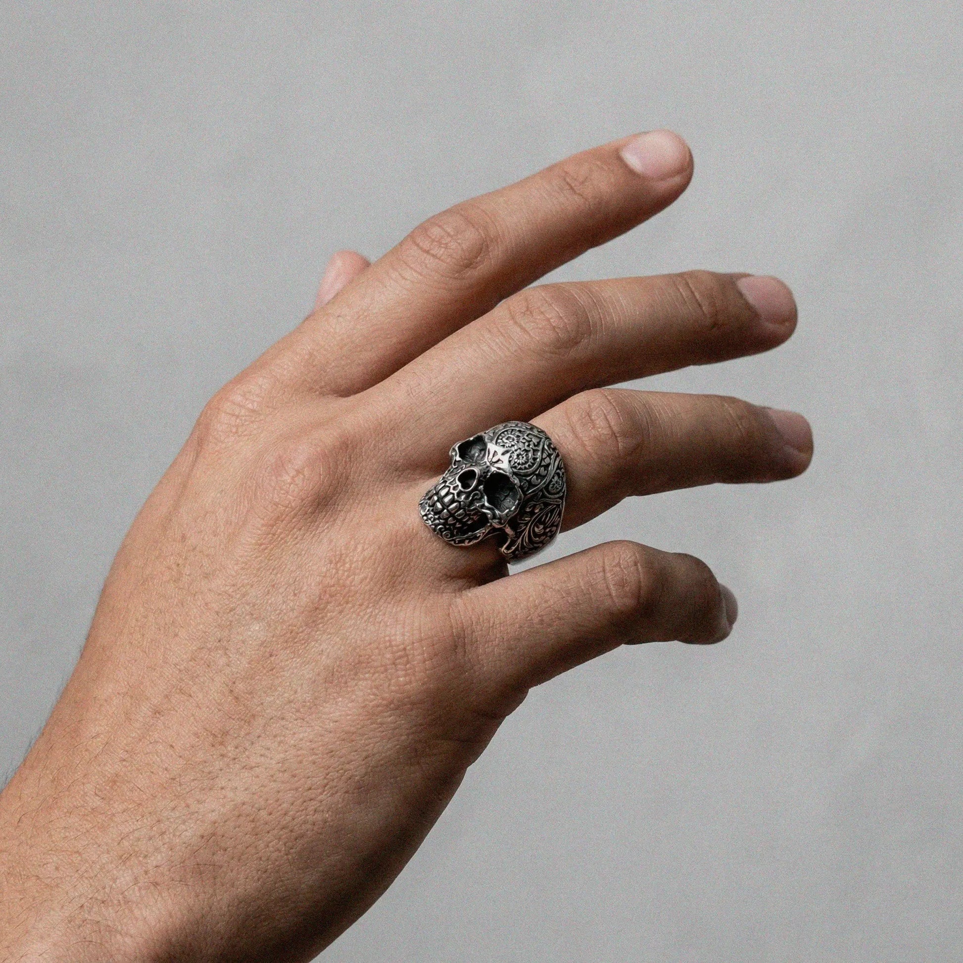 Hand wearing a silver mexican skull ring on a plain background