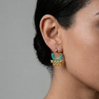 Gold aztec earring with turquoise accent worn by a person against a gray background