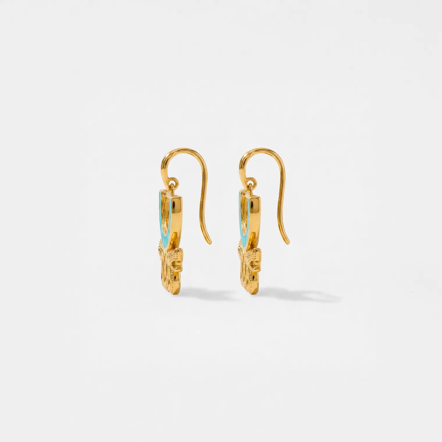 Gold aztec earrings with turquoise stones on a light gray background