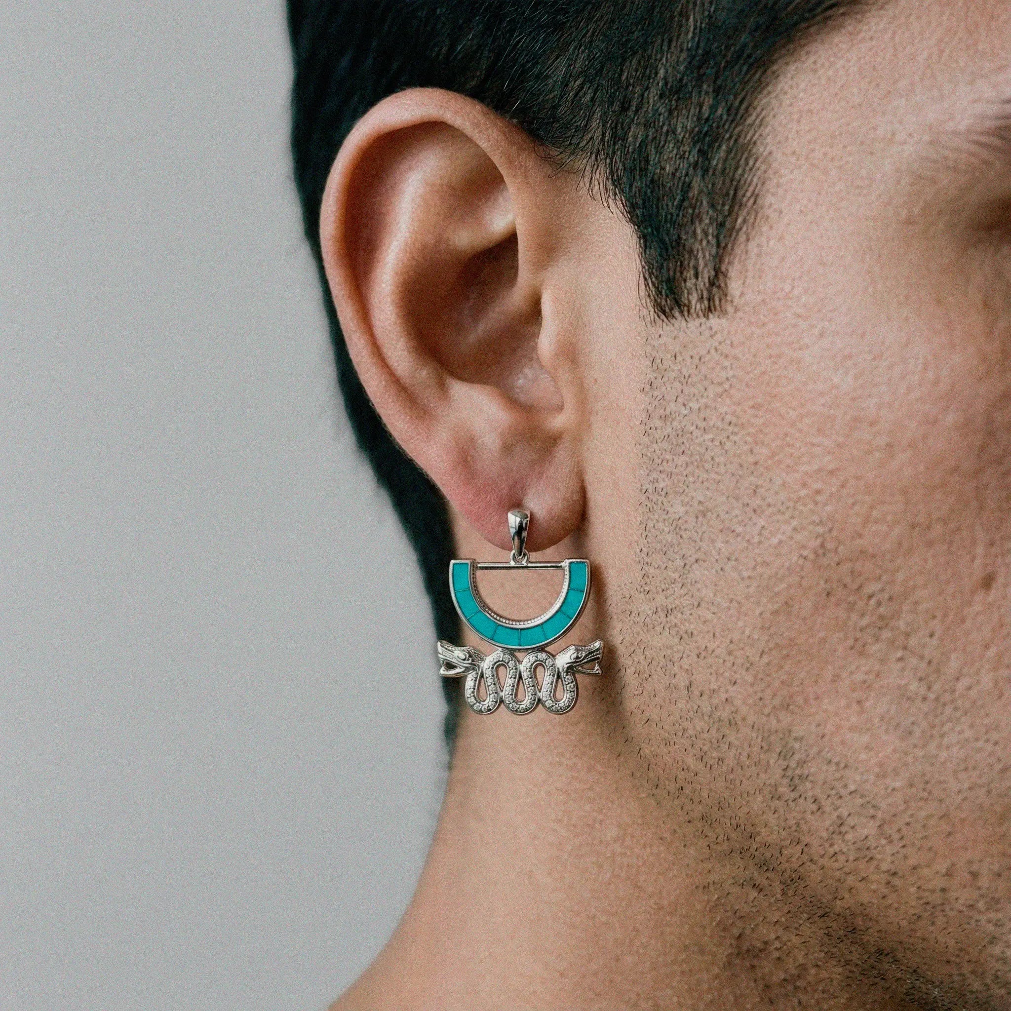Close-up of an ear wearing a turquoise and silver aztec earring against a neutral background