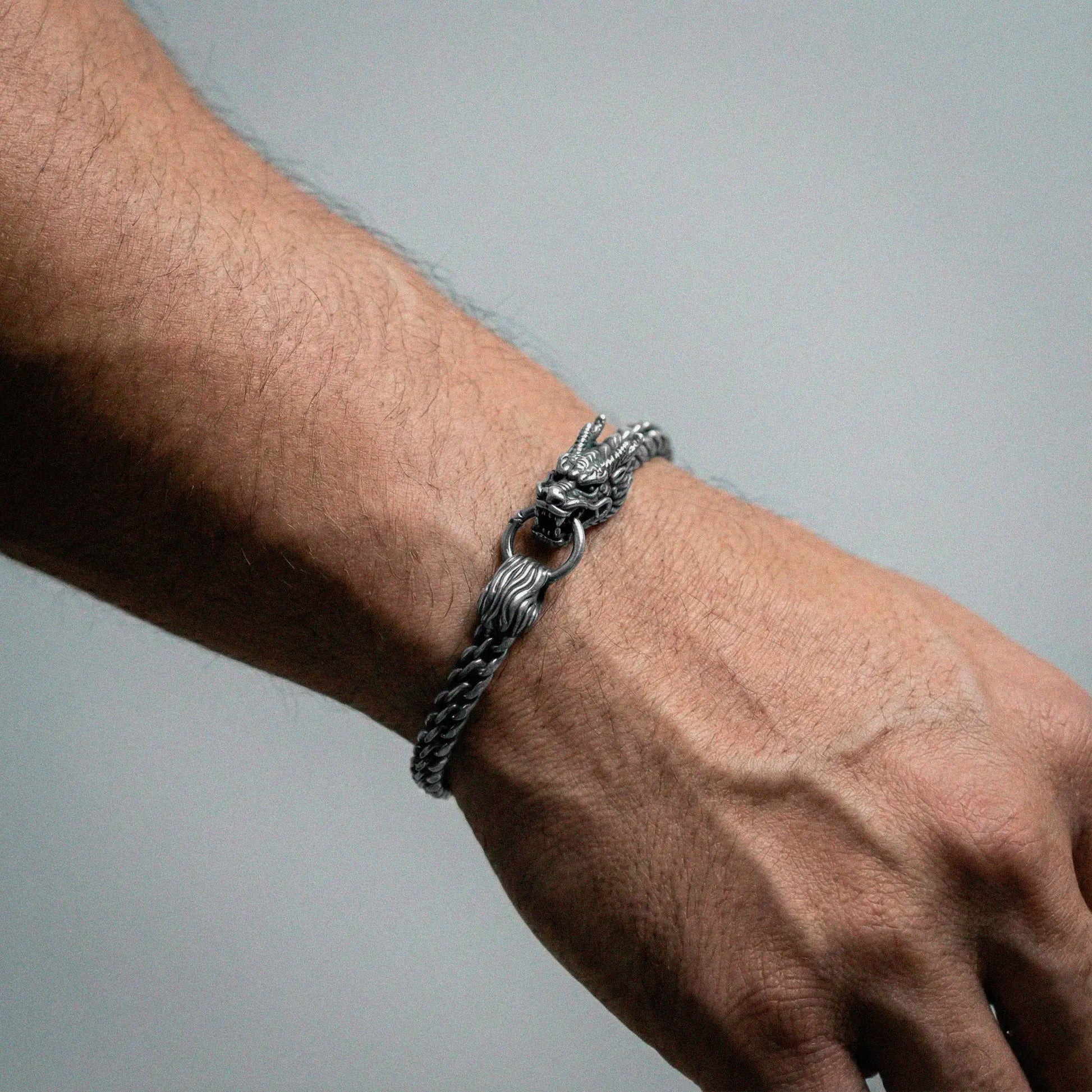 Silver chain bracelet on a wrist against a gray background