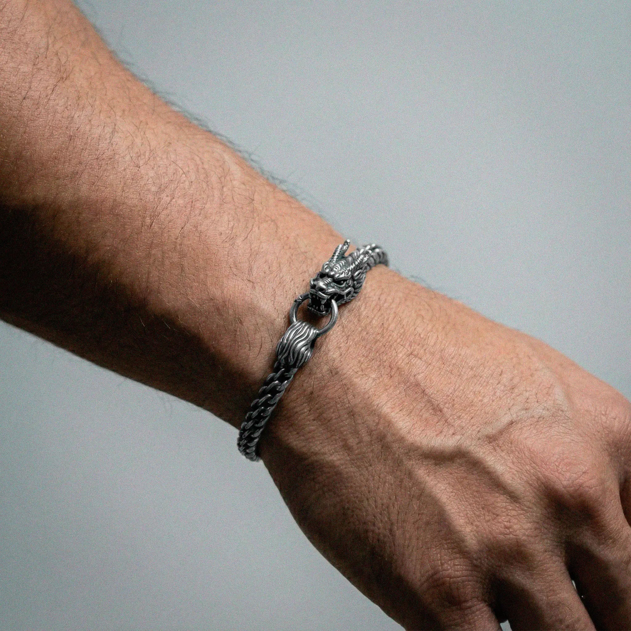 Silver chain bracelet on a wrist against a gray background