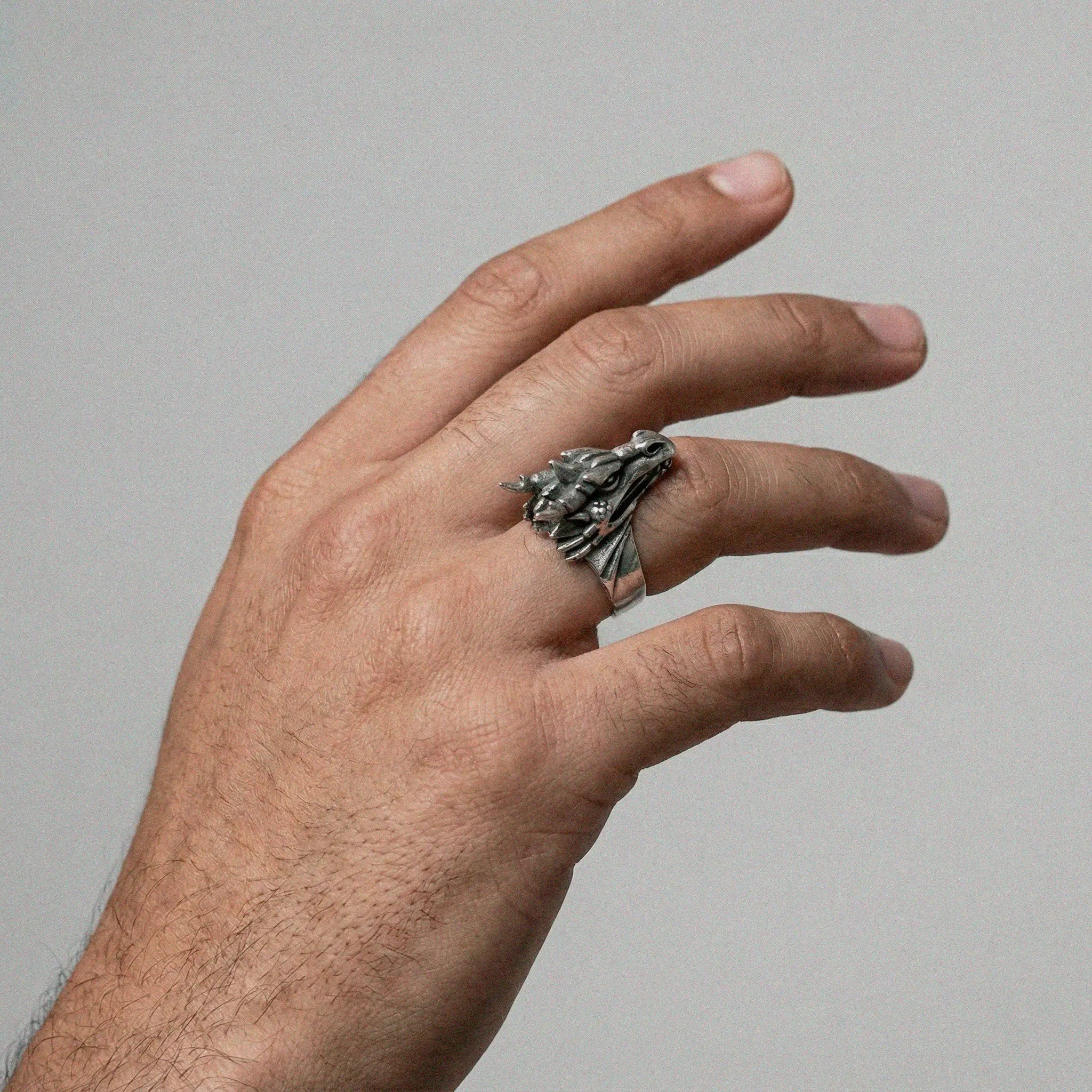 Hand wearing a silver ring with a DRAGON design on a plain background