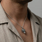 Silver necklace with an eagle head pendant worn by a person in a beige shirt.