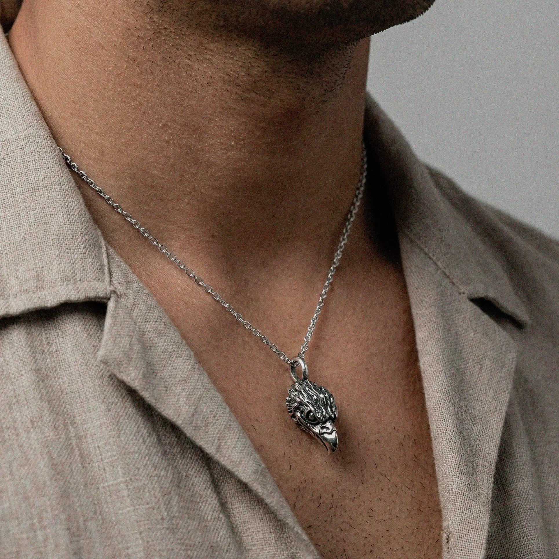 Silver necklace with an eagle head pendant worn by a person in a beige shirt.