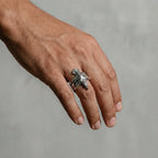 Hand wearing a silver ring with an eagle design on a neutral background